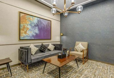 Modern lounge area with a grey velvet sofa, abstract art, and a decorative gold chandelier.
