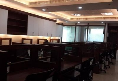Modern workspace with rows of dark wood desks, white cabinetry, and recessed ceiling lighting.