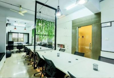 Coworking space featuring white desks, black chairs, and hanging green plants.