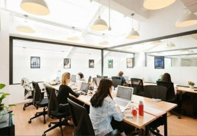 Bright open-plan office with long wooden desks, ergonomic chairs, and large glass partitions.