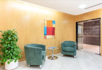 Waiting area with two teal velvet armchairs, a glass side table, and a large potted plant.