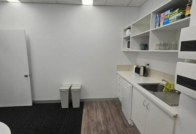 Communal kitchen area with white cabinetry, wood-look flooring, and a sink.