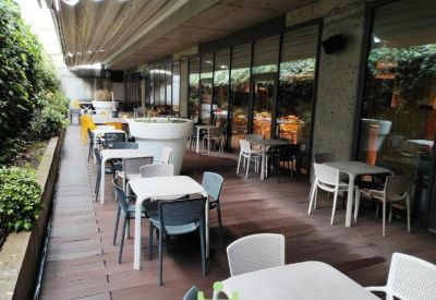 Outdoor terrace with white tables and grey chairs surrounded by greenery.