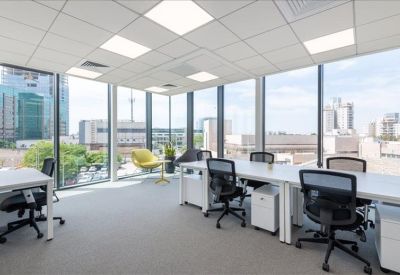 Open-plan office space with white desks, ergonomic black chairs, and panoramic window views.