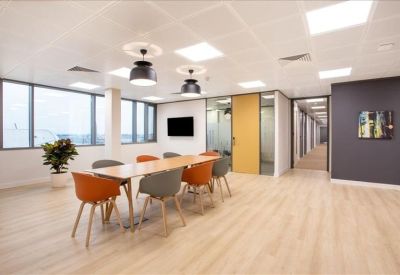 Open-plan dining area with a long wooden table, orange and grey chairs, and large windows.