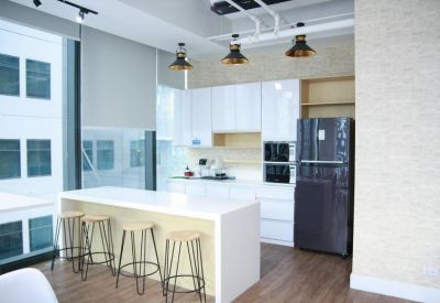 Modern communal kitchen with a breakfast bar, stools, white cabinetry, and large windows.