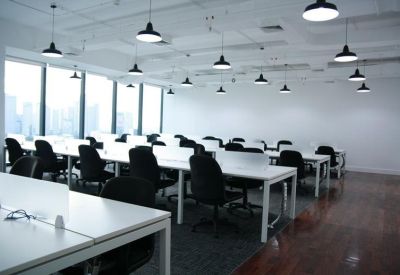 Bright open-plan office with white desks, black chairs, and hanging pendant lights.