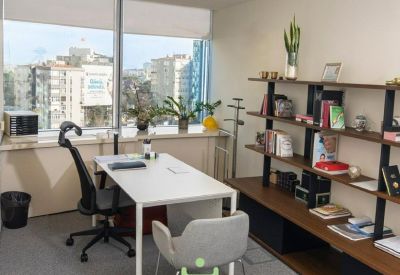 Private office with white desk, ergonomic chair, and city views through large windows.