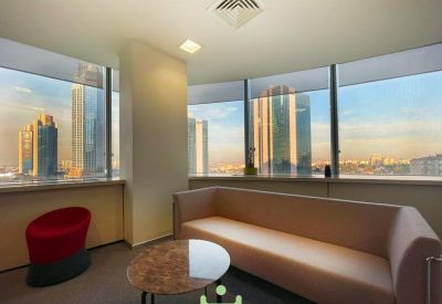 Bright lounge area featuring a long tan sofa and a modern red accent chair by the window.