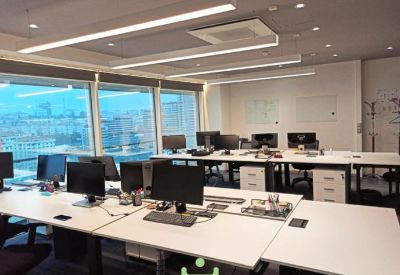Spacious open-plan workspace with multiple desks and city views through large windows.