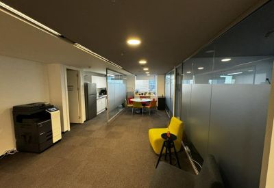 Breakout area with a yellow armchair, a printer station, and a kitchen in the background.