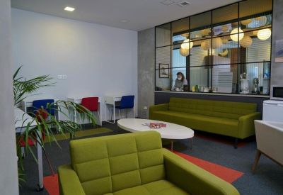 Vibrant breakroom with green sofas, colorful chairs, and a glass partition wall.