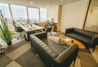 Executive office with black leather sofas, a wooden desk, and a large window view.