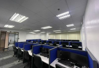 Open-plan office space featuring rows of blue-partitioned workstations and bright overhead lighting.