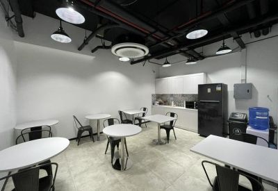Breakout area with white tables, black chairs, and a kitchenette featuring a refrigerator.