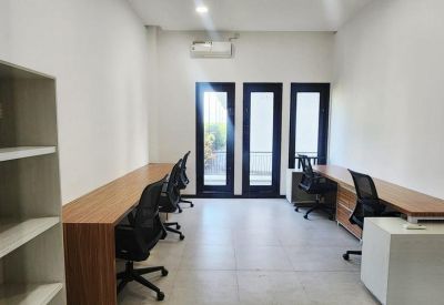 Brightly lit office with desks facing a set of three vertical windows.