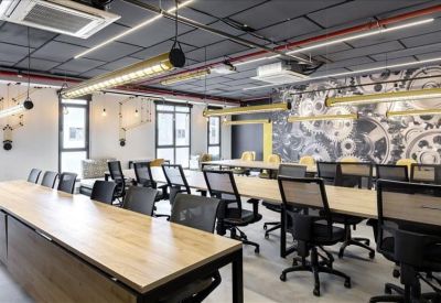 Open-plan coworking space with long wooden desks and black ergonomic chairs.