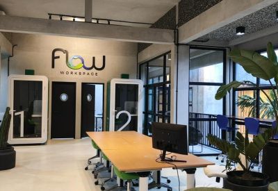 Spacious open-plan coworking area with wooden communal tables and green armchairs.