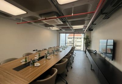 Long boardroom with a light wood table, grey chairs, and a flat-screen TV.