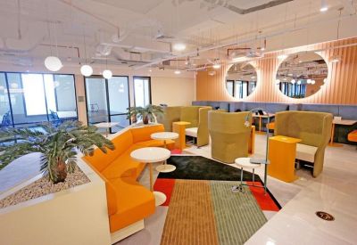 Bright coworking lounge with orange sofas, green pods, and circular mirrors.