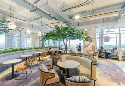 Spacious communal lounge featuring curved booth seating, indoor trees, and exposed ceiling pipes.