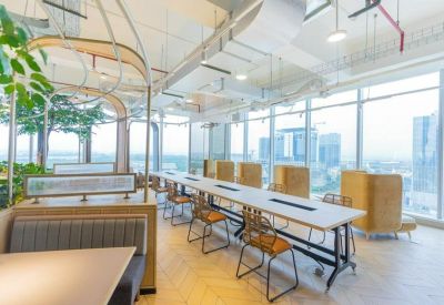 Modern coworking area with a long shared wooden table, industrial ceilings, and floor-to-ceiling windows.