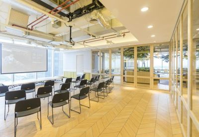 Bright seminar room with rows of black chairs facing a projector screen and glass walls.