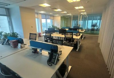Spacious open-plan workspace with multiple white desks, ergonomic chairs, and large windows.
