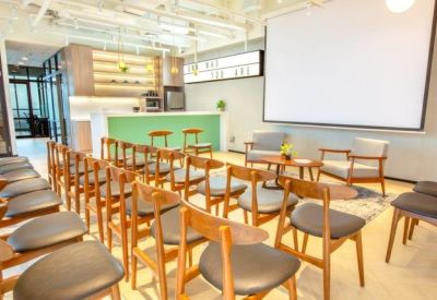 Spacious event room with rows of wooden chairs facing a large projection screen and stage area.