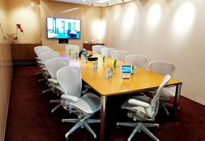 Spacious boardroom featuring a light wood table, mesh chairs, and a wall-mounted TV.