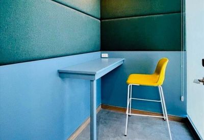 Private phone booth featuring sound-absorbing green wall panels and a bright yellow high-back chair.