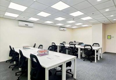 Open-plan office space with rows of white desks, black mesh chairs, and bright panel lighting.