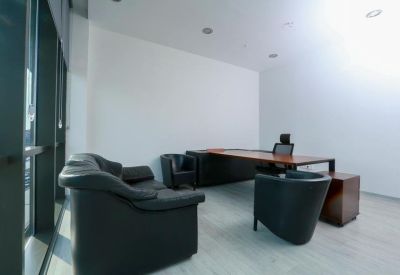 Private office featuring a large wooden desk and black leather sofa with bright natural light.