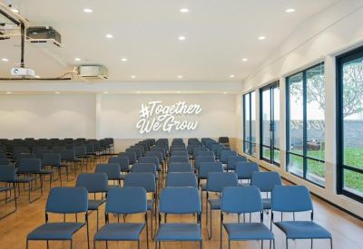 Large presentation room with rows of blue chairs and a lit wall sign.