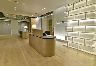 Minimalist reception area with a curved wooden desk and a geometric illuminated wall shelf.