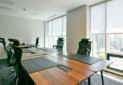 Bright office room with several wooden desks, ergonomic chairs, and large windows.
