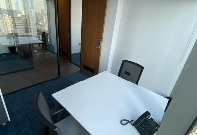 Bright private corner office with a white desk and city views through glass partitions.