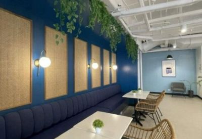 Colorful breakout area with a long blue banquet, white tables, and hanging plants.
