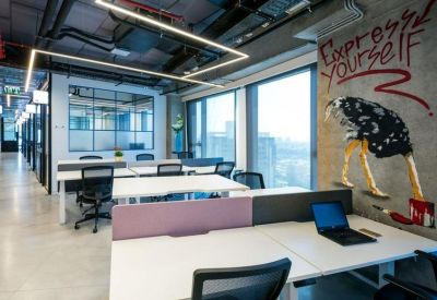 Bright open-plan office space with white desks and a large colorful wall mural.