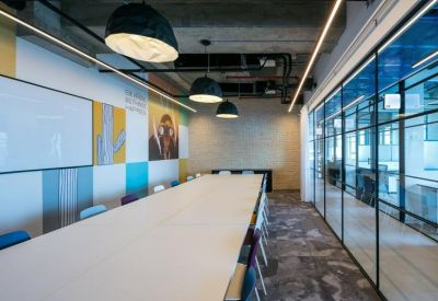 Modern meeting room with a long white table, colorful wall panels, and large glass walls.