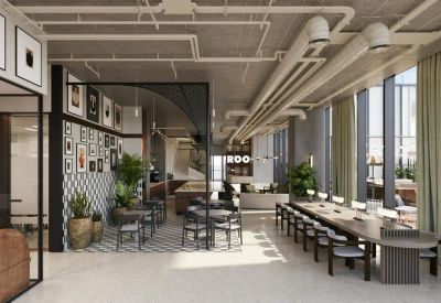 Open-plan coworking space with long communal tables, industrial piping, and large windows.