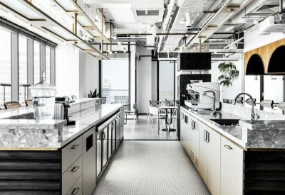 Bright modern kitchen with marble islands, professional espresso machine, and exposed ceiling pipes.
