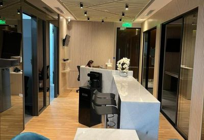 Modern lobby area with a marble reception counter, turquoise velvet chairs, and a slatted wood ceiling.