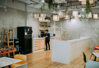 Modern communal kitchen and cafe area with light wood floors and a long white breakfast bar.