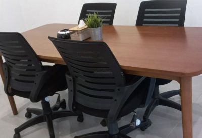 Close-up of a wooden meeting table with black ergonomic mesh chairs and a small potted plant.