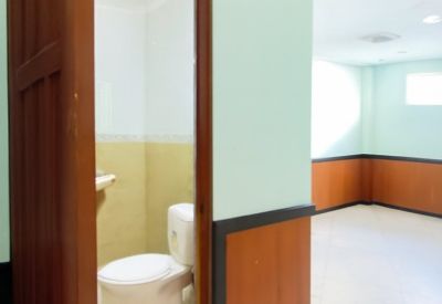 View through a dark wood door into a bathroom with a white toilet and tan wall tiles.