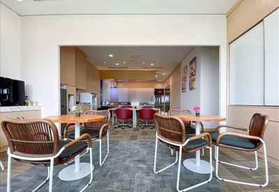 Spacious breakout area with wooden tables and woven chairs looking into a workspace.