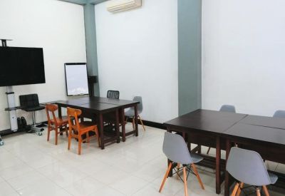 Spacious training room with a large wall-mounted screen, whiteboard, and dark wood tables.