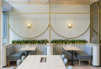 Modern dining area with light wood tables, blue banquette seating, and gold geometric wall accents.