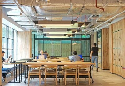 Bright open-plan workspace featuring long wooden tables and ergonomic chairs under industrial light fixtures.